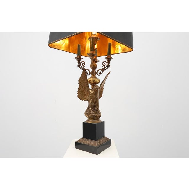 A Hollywood Regency table lamp by the Belgian maker Deknudt, crafted around 1980 and featuring a dramatic sculptural eagle...