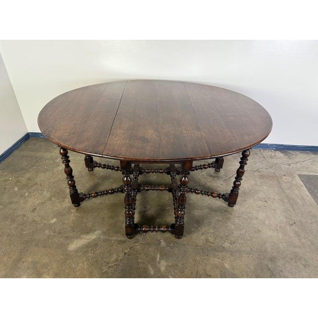 This is a 19th century English gateleg drop-leaf table crafted from dark-stained oak. The oval top features two hinged...