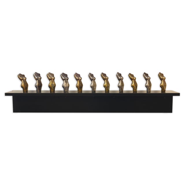 Striking contemporary wall-mounted sculpture featuring a row of eleven cast nude torsos in alternating bronze and silver-...
