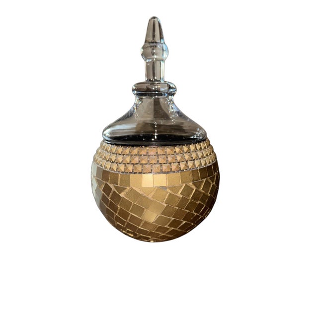 A striking gold mosaic glass decorative jar featuring a rounded silhouette and an elegant clear glass lid with sculptural...