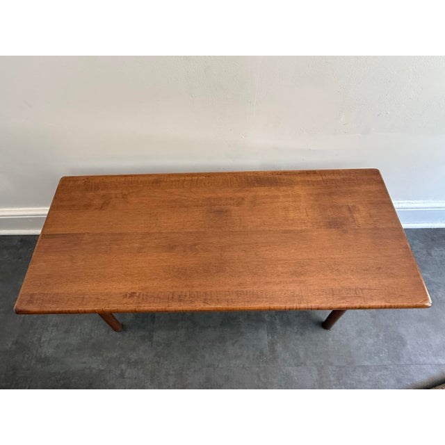 A mid-century modern solid wood coffee table with rounded corners, tapered splayed legs, and an H-stretcher with ribbed...