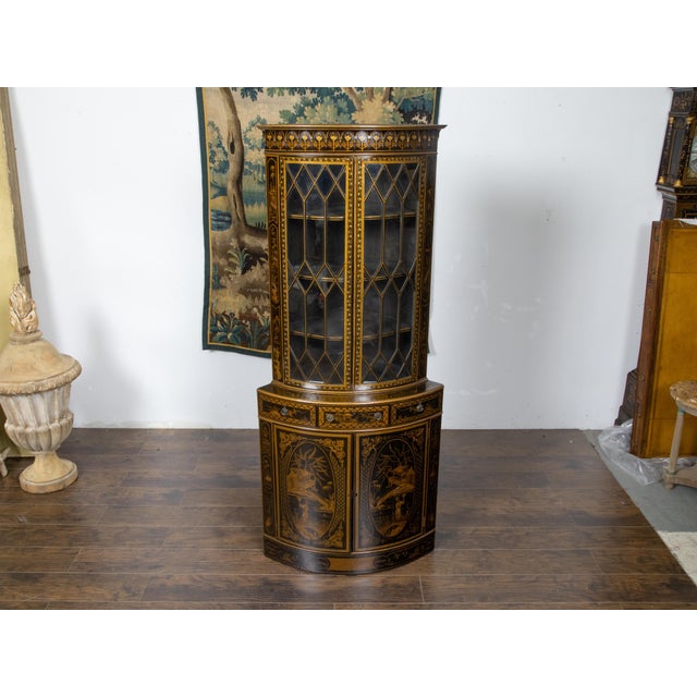 An English black and gold corner cabinet from the 19th century, with paneled glass doors, three middle drawers and...