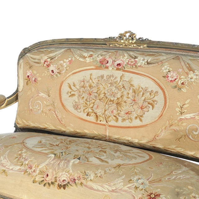An antique French Louis XV style sofa offers giltwood frame with carved crest over Aubusson tapestry upholstered back and...
