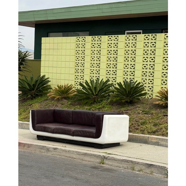 A modernist space age sofa after William Andrus, circa 1970. White shell with aubergine hued leather, which appears...