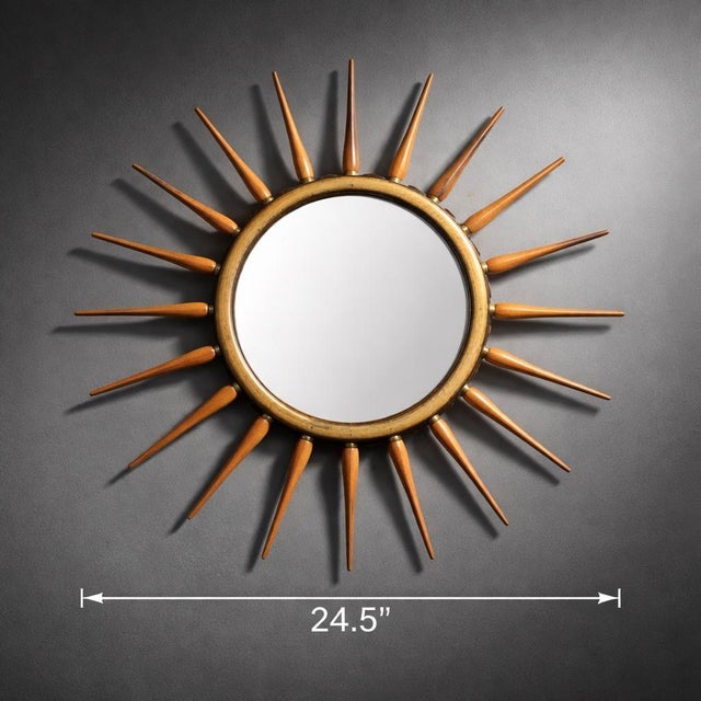 A sculptural Mid-Century Modern style sunburst mirror featuring a warm wood frame and tapered orange spindle rays with...