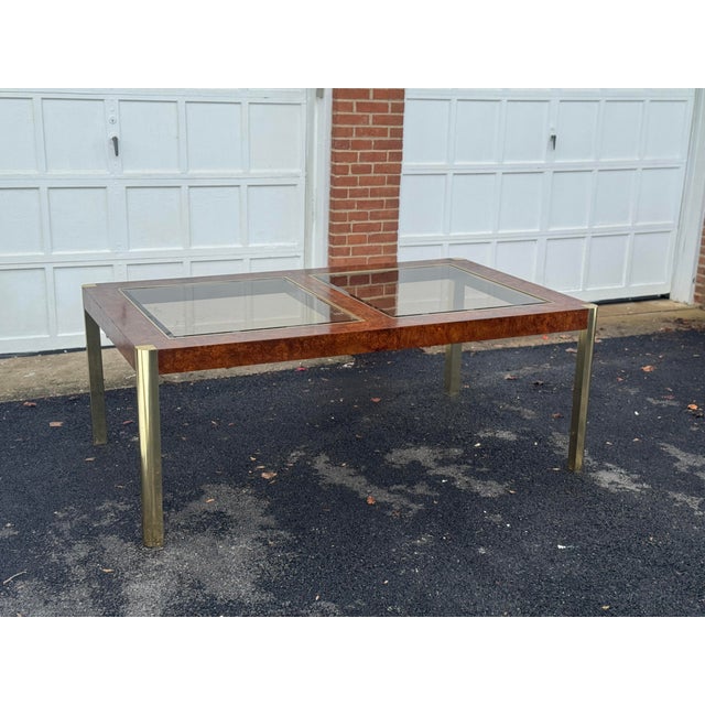 A refined vintage coffee table featuring a richly figured burl wood top framed by polished brass legs. The tabletop...