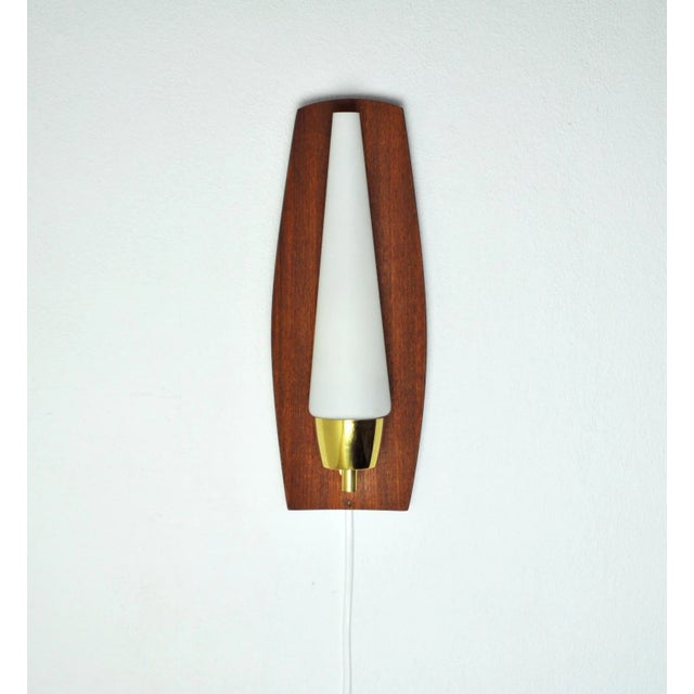 Mid-Century Modern wall light in a slightly bowed teak, brass and opaline glass shade. Probably made in Denmark the 1960s....