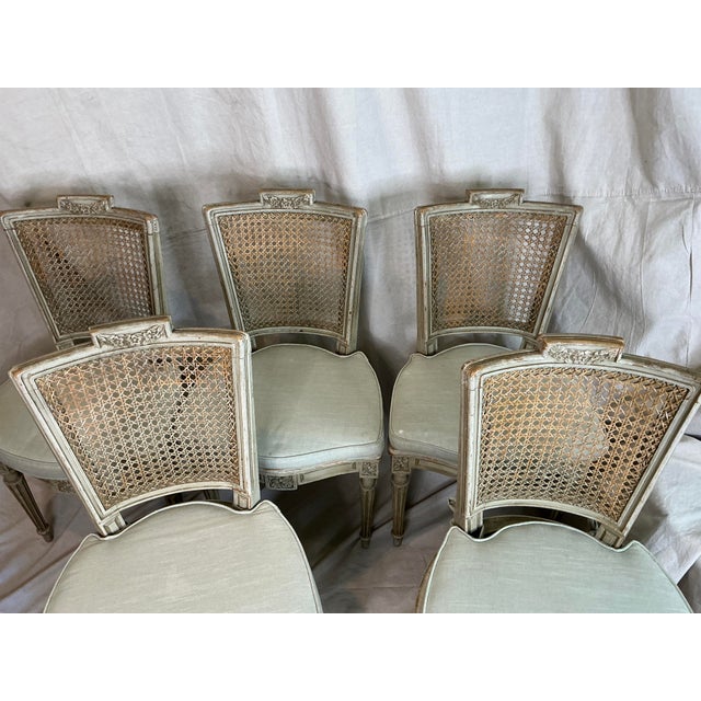 Elegant set of five French Louis XVI style dining chairs featuring hand-caned backs, carved floral details, and fluted...