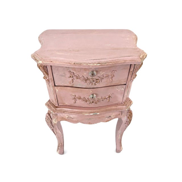 A beautifully restored French nightstand in a soft, romantic pink with a gently distressed finish. This piece features...