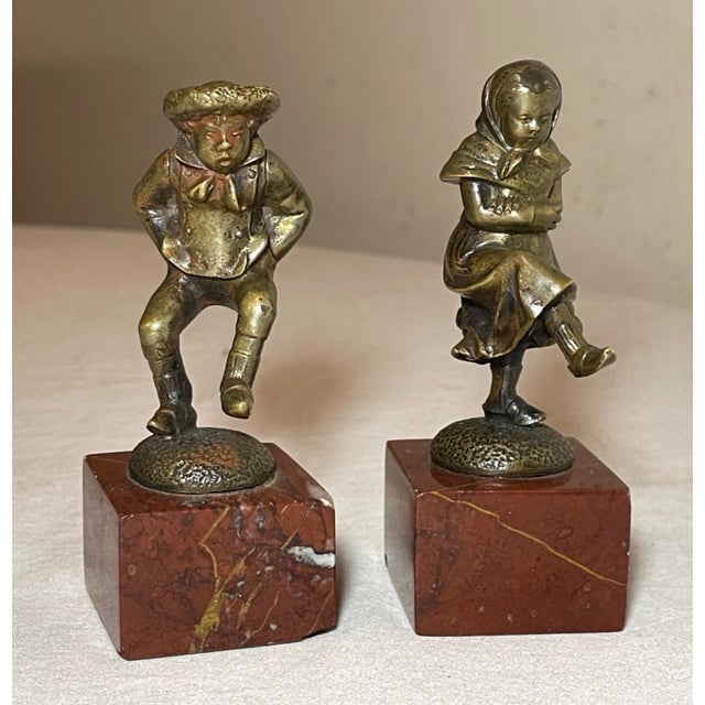Crafted with meticulous attention to detail, this pair of bronze statues portrays a charming scene of a young boy and girl...