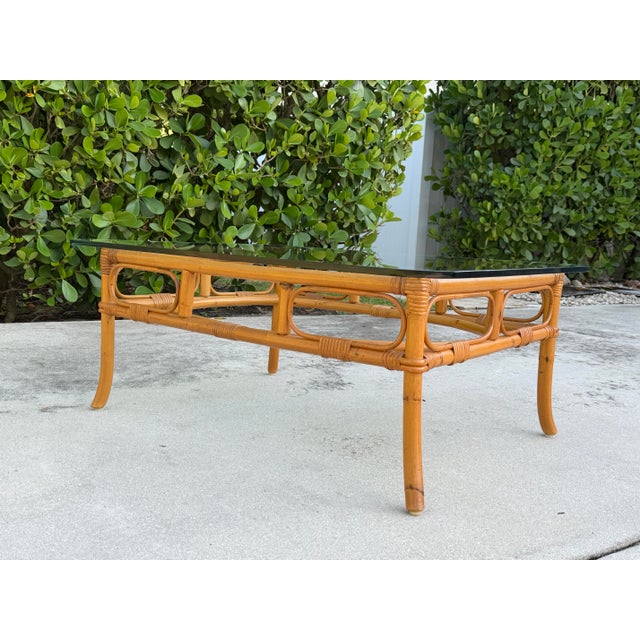 Striking vintage coffee table featuring an elaborate bamboo-style rattan frame with sculptural curved supports, wrapped...