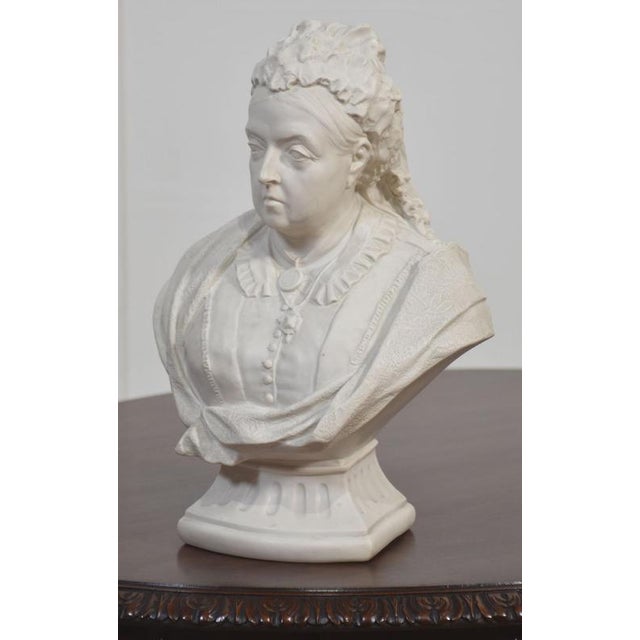 Parian bust depicting Queen Victoria in later life, shown wearing formal dress with lace-trimmed bodice, shawl, and...