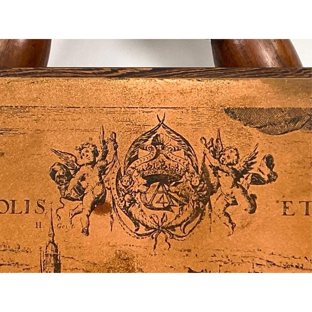 A long, rectangular engraved copper wall plate mounted on a dark wood backing depicting a panoramic bird's-eye view of...