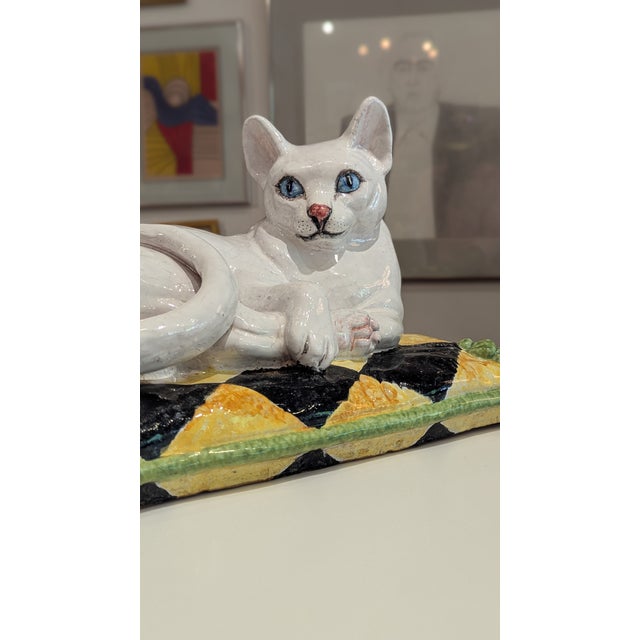 Glossy white ceramic cat reclining atop a patterned pillow base with tassel detailing. Italian export, c. 1960s–70s.