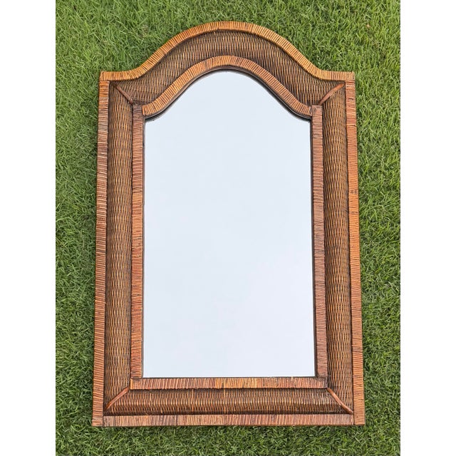 Vintage wall mirror featuring a distinctive serpentine-shaped crest and intricately woven rattan frame. The warm natural...