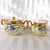 This is a cream and gold sugar bowl with lid and matching creamer. They have purple and blue flowers and greenery all...