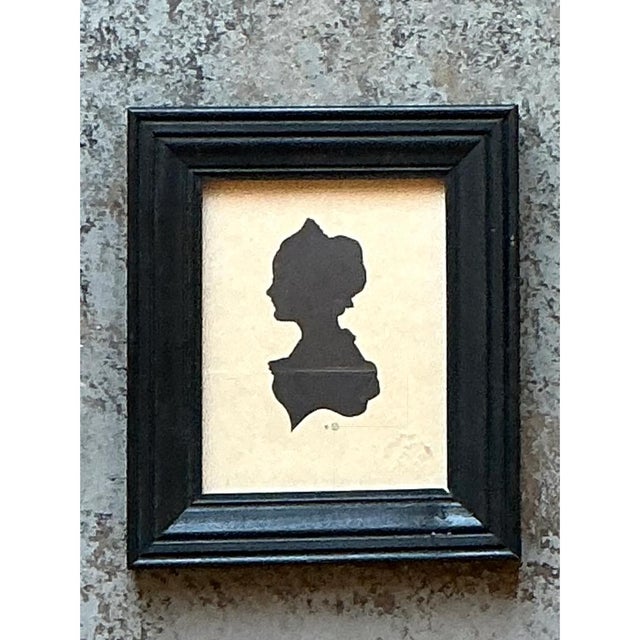 This vintage miniature portrait is a graceful profile silhouette of a woman facing left, cut in solid matte black paper...