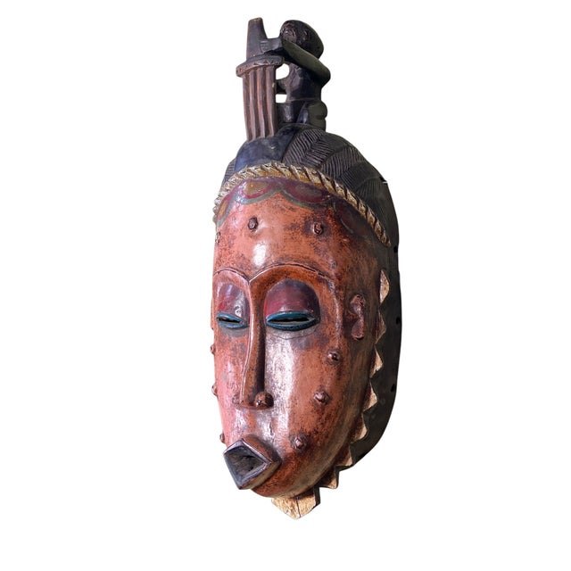 This Unique African Guro mask from Côte d'Ivoire features a female figure with a comb in her hair and a seated male on...