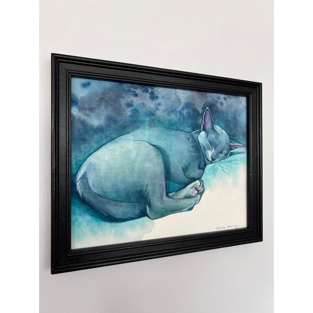 The artwork depicts a serene, sleeping cat, rendered in soft shades of blue and gentle washes of color that evoke a...
