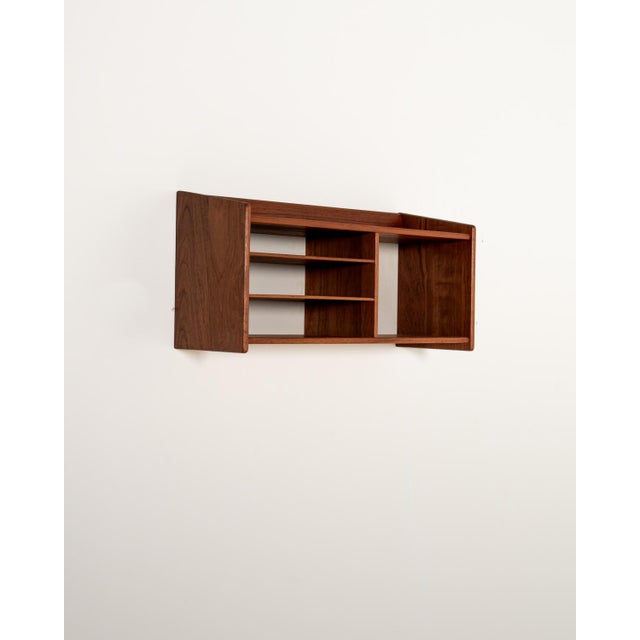 Teak wall shelf featuring asymmetrical open compartments, with two thin shelves on the left side and a larger compartment...