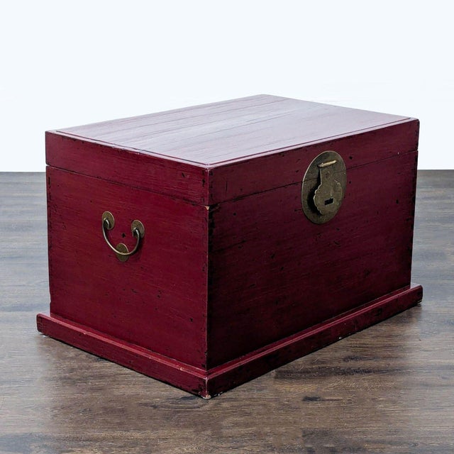 This wooden trunk features a deep red finish and metal hardware. It has a hinged lid and sturdy side handles for easy...