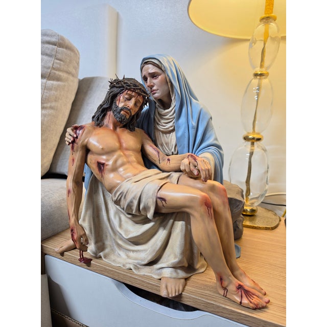 This religious sculpture represents the Virgin Mary holding Jesus in the traditional Pietà composition, capturing a moment...