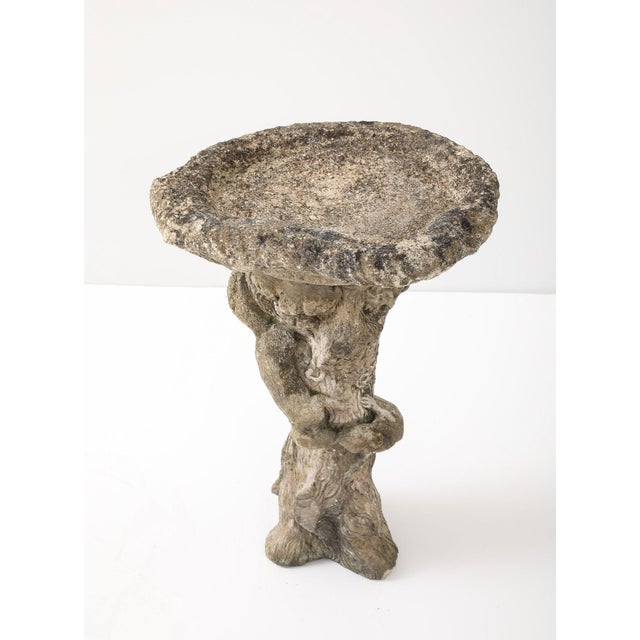 An English mid-20th-century composite stone birdbath, with a textured, hollowed-out log basin, rests atop a pedestal...