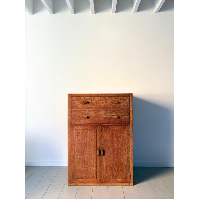 An early 20th century limed oak tallboy cabinet by heals of london. This 1930s vintage wooden cupboard has a shelved...