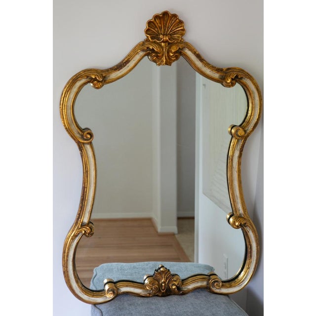 Rococo vintage gold gilt wall mirror. It has a beautiful hour glass shape, with ornate c-scrolls, acanthus leaves and a...