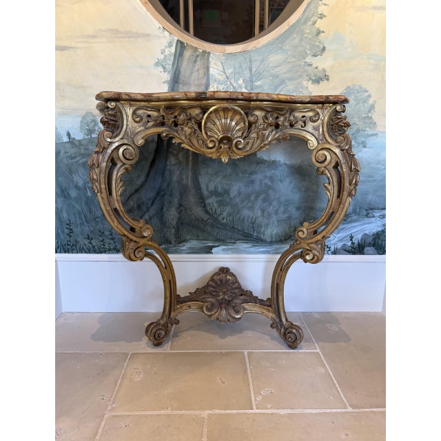 Italian Rococo style console table featuring a richly carved giltwood base adorned with scrolling acanthus leaves, shell...