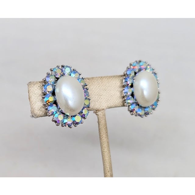 Circa 1953 to 1955 rhodium plated oval faux-pearl with round blue aurora borealis accents surround clip earrings. Marked...