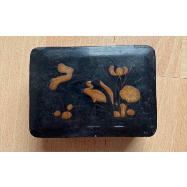 Small, black lacquered box measuring approximately 3.9 × 9.2 × 6.9 cm (H/W/D). The lid is decorated with a gold and bronze...