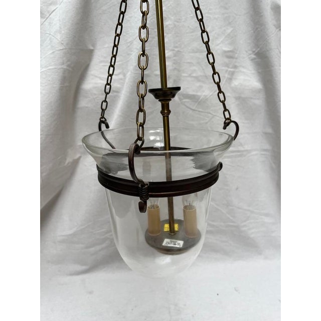 A single vintage metal ceiling light featuring a transparent glass bell shaped globe suspended by three metal chains and a...