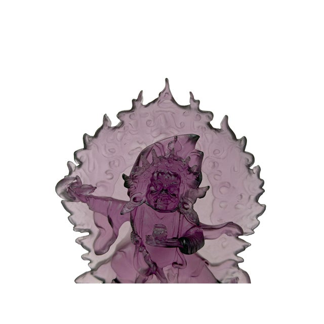 This striking art piece features a translucent, deep amethyst-purple molded glass sculpture of a dynamic deity or wrathful...