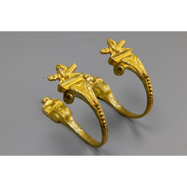Elegant French Empire–style gilt bronze curtain tiebacks with classical ornament, late 19th century. A refined pair of...