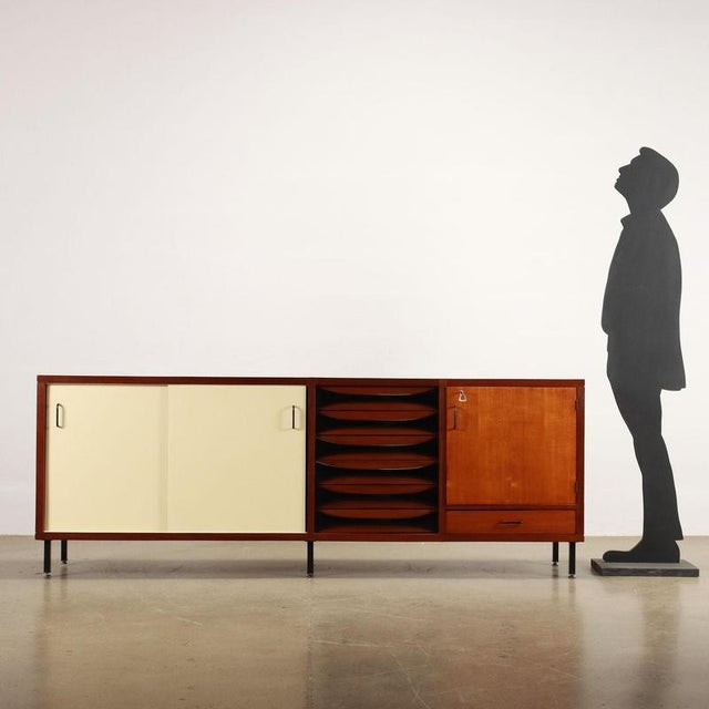 Sideboard with sliding doors, one hinged door, and open drawers in teak veneer and Formica with enameled metal legs. This...