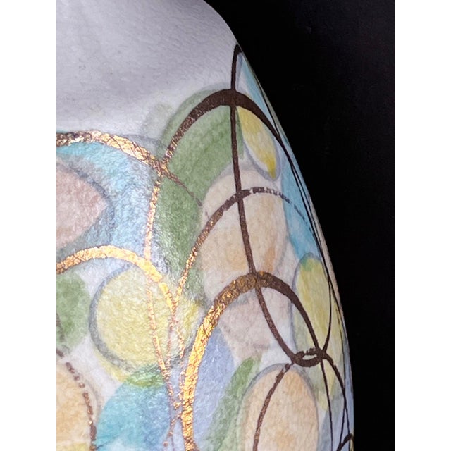 each colorful bottle-form lamp adorned with painted circles in soft colors of blue, green, peach and yellow with a gold...