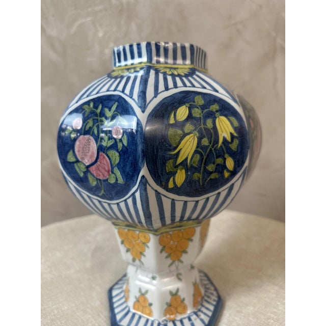 An elegant earthenware vase with a rounded body, resting on an octagonal base. Its decoration combines blue and white...