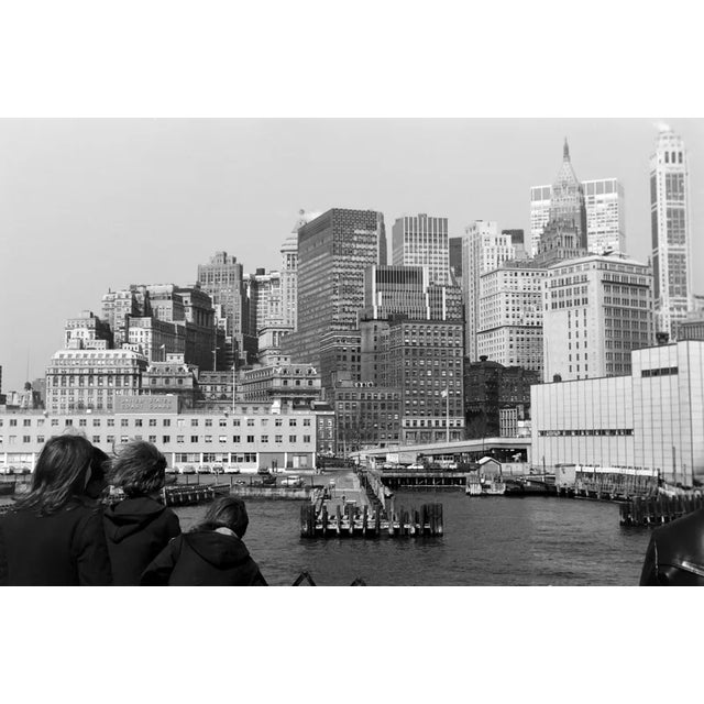 This black-and-white photograph offers a captivating view of New York Harbor, with the towering skyline of Lower Manhattan...