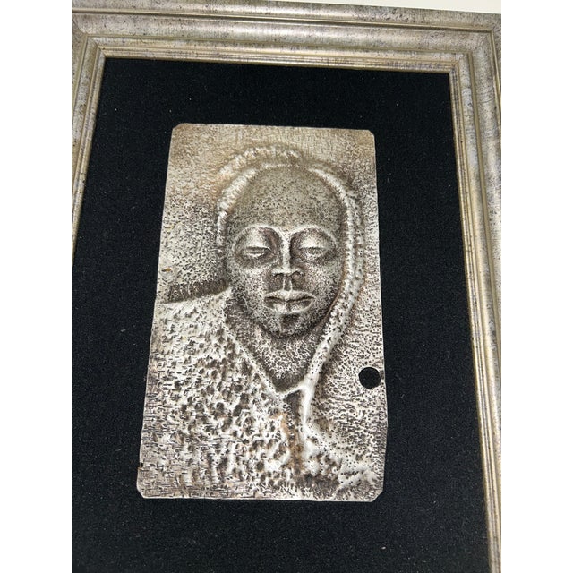 A striking zinc metal relief wall sculpture featuring an African-inspired portrait, presented in a refined silver frame...