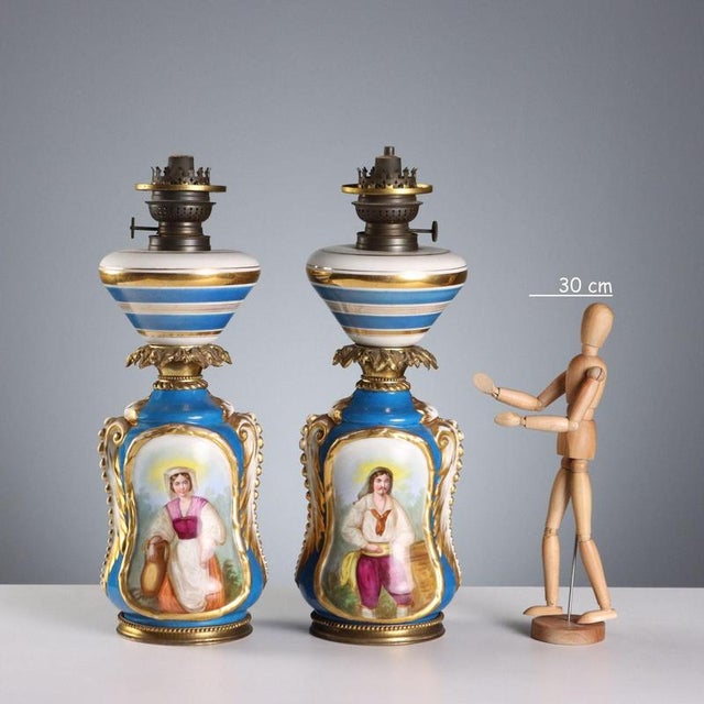 A pair of ceramic lamps painted in polychrome with bold gold highlights. The reserves feature floral arrangements and...