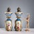 A pair of ceramic lamps painted in polychrome with bold gold highlights. The reserves feature floral arrangements and...