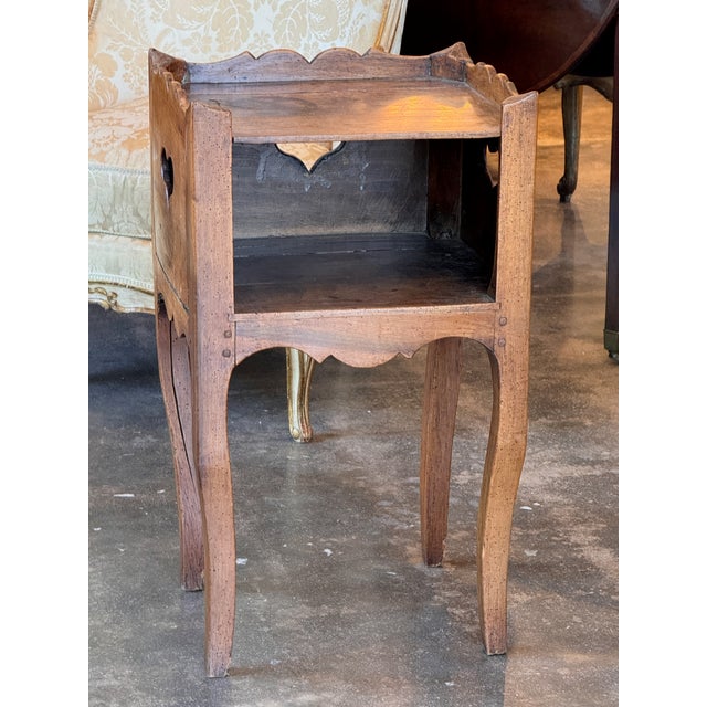 A simple country French side table with a scalloped gallery top, open shelf, and heart-shaped cutouts to the sides....