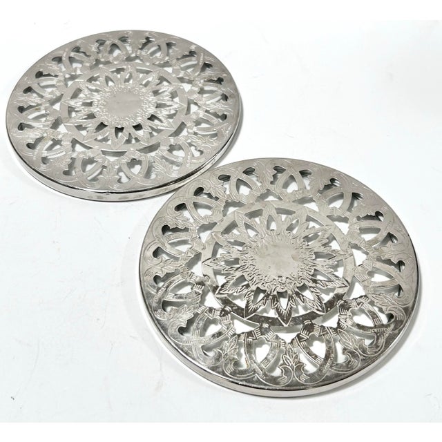 1960s silver-plated trivets featuring an ornate pierced sunburst motif, a classic mid-century tabletop accessory that...