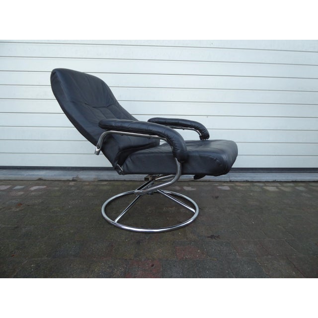 This vintage easy or lounge chair features black faux leather upholstery and a chrome plated base. Stamped by Maker