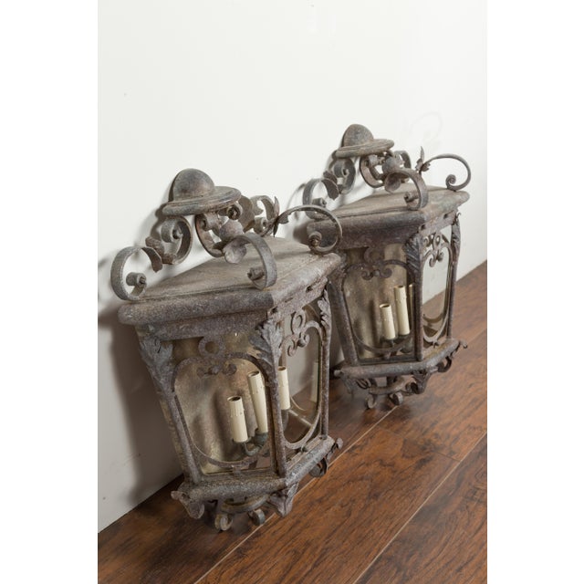 A pair of French iron lanterns from the early 20th century, with three lights and scrolling motifs. Created in France...