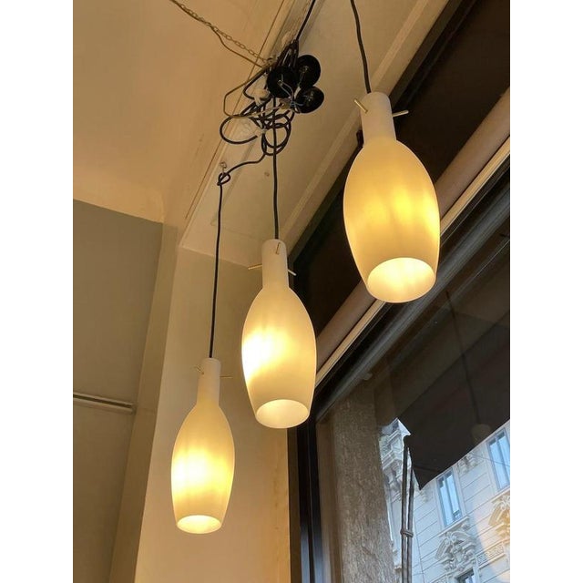 1960s glass pendant lights. Each fixture features three satin white opaline glass diffusers, enhanced by brass details at...
