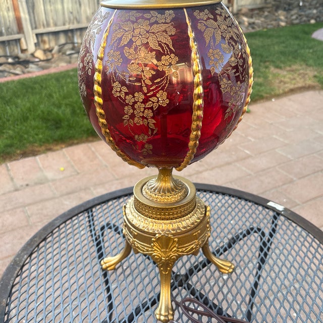 Stunning mid-century Hollywood Regency table lamp featuring a vibrant ruby red ribbed glass globe body adorned with...