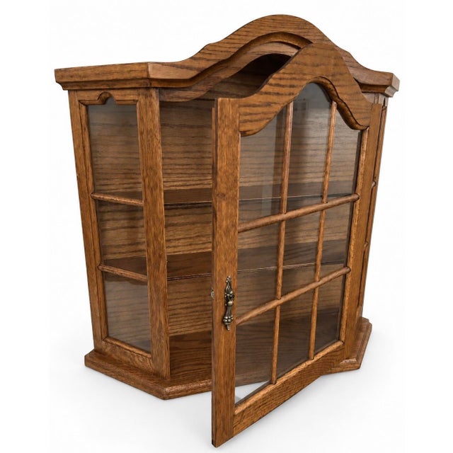 Vintage wall-mounted oak curio cabinet featuring an architectural arched crown, divided transparent panels, angled sides,...