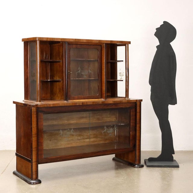 Showcase with hinged door and sliding doors, open shelves. Walnut veneered wood. This piece is attributed to the mentioned...